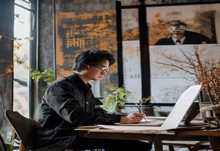 林宇，秋色之空创始人与创意总监，在工作室内专注审视品牌方案，背景是大幅视觉草稿，神情沉稳自信
